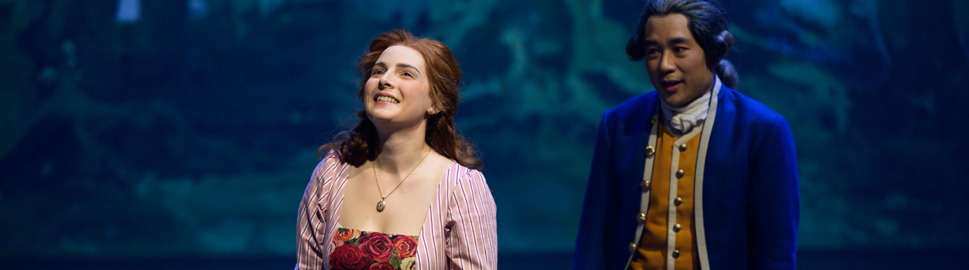 Das Bild zeigt eine junge Frau und im Hintergrund einen jungen Mann, beide in Kostümen der Goethezeit.