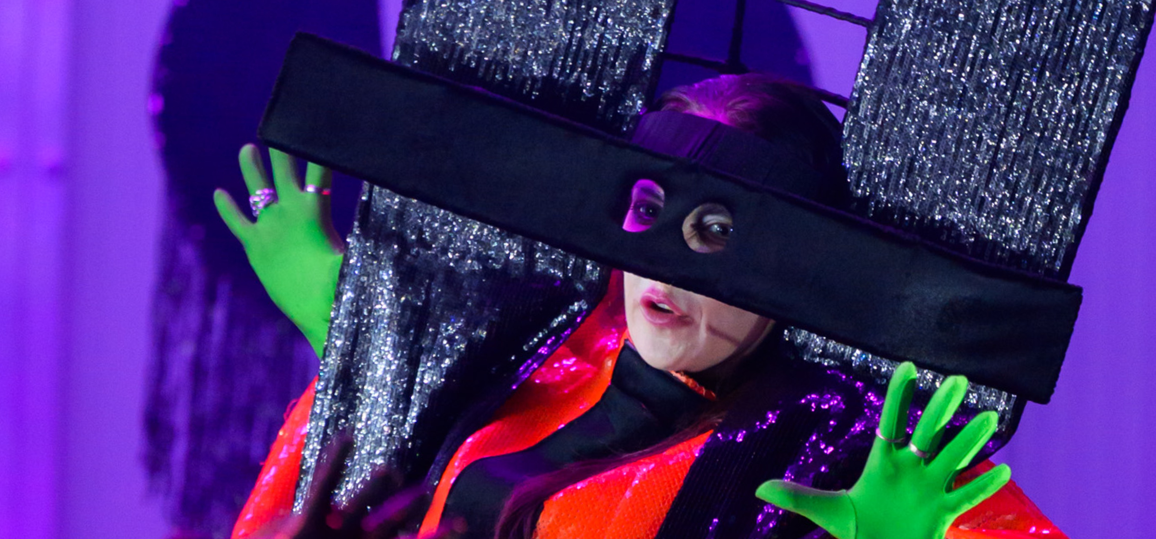 Auf rotem Untergrund stehen die Buchstaben D N T. Im Umriss der Buchstaben ist eine Frau mit grünen Handschuhen und einem schwarz-roten Kostüm zu sehen.