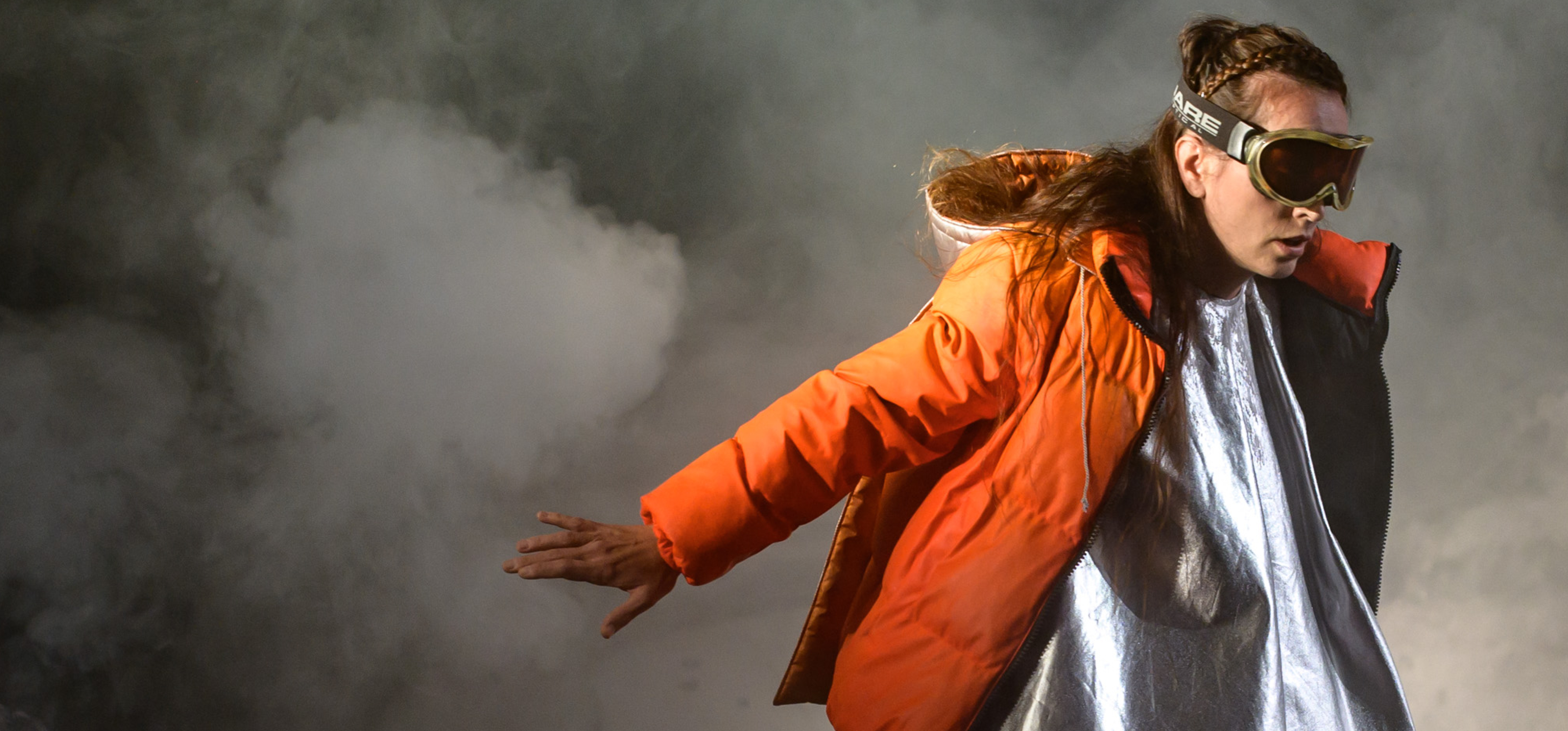 Auf rotem Untergrund stehen die Buchstaben D N T. Im Umriss der Buchstaben ist eine Frau mit Skibrill und einem orangefarbenen Mantel zu sehen.